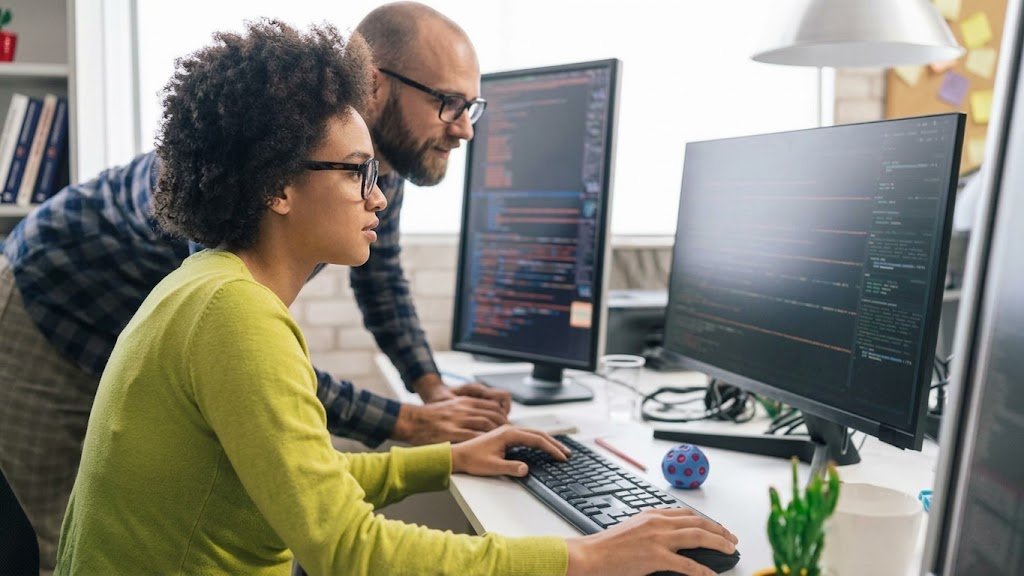 Two developers reviewing code together on large monitors in a bright office